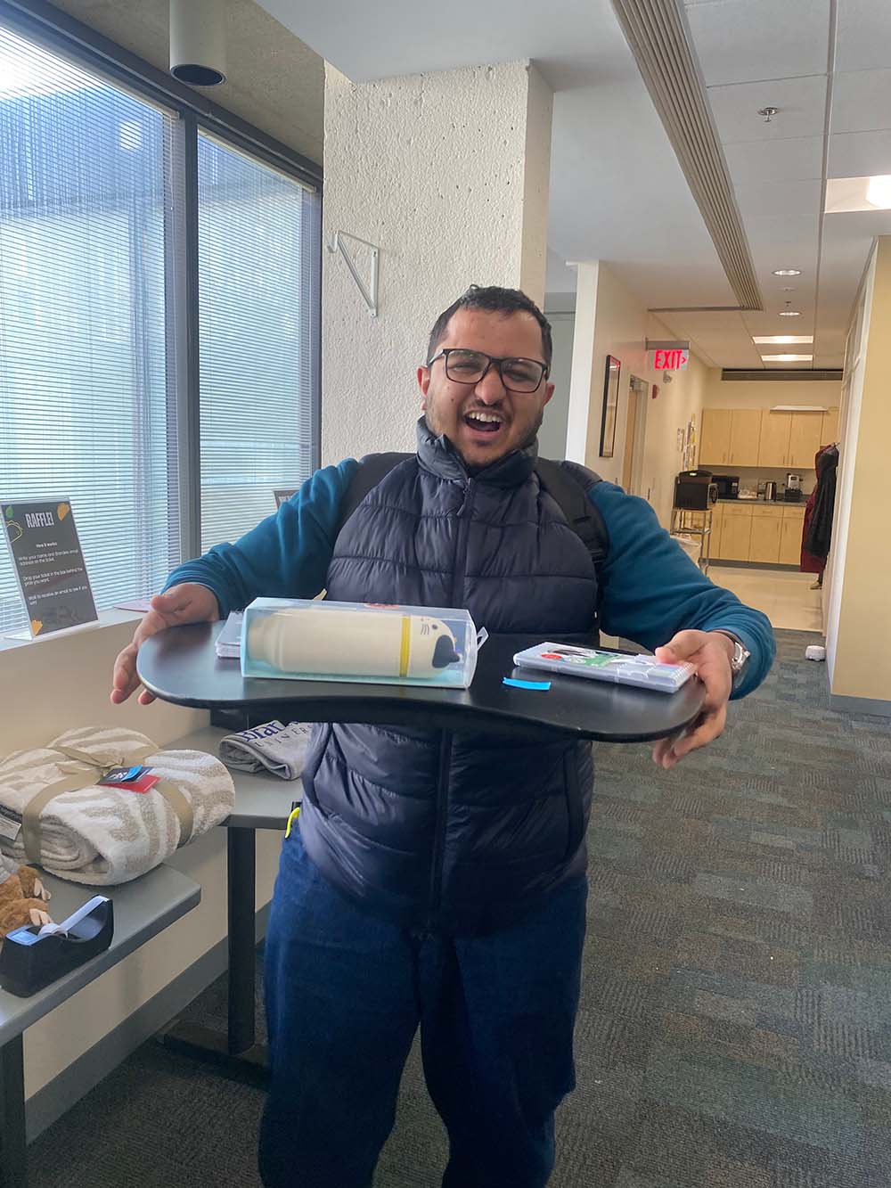 A student grins broadly while holding a tray with a water bottle on it.