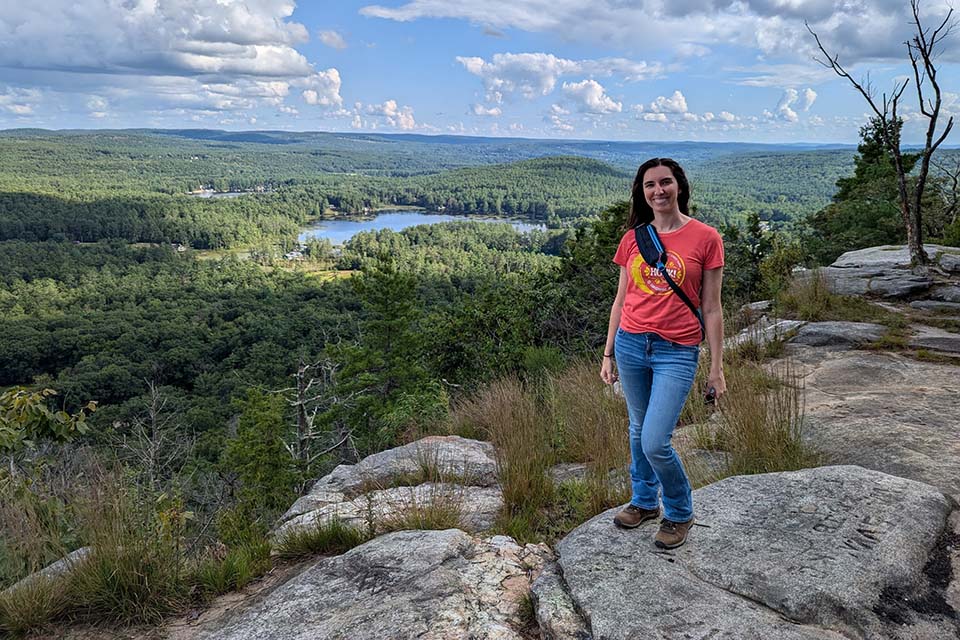 Jamie Brandon stands on rocks overlooking trees and a lake.