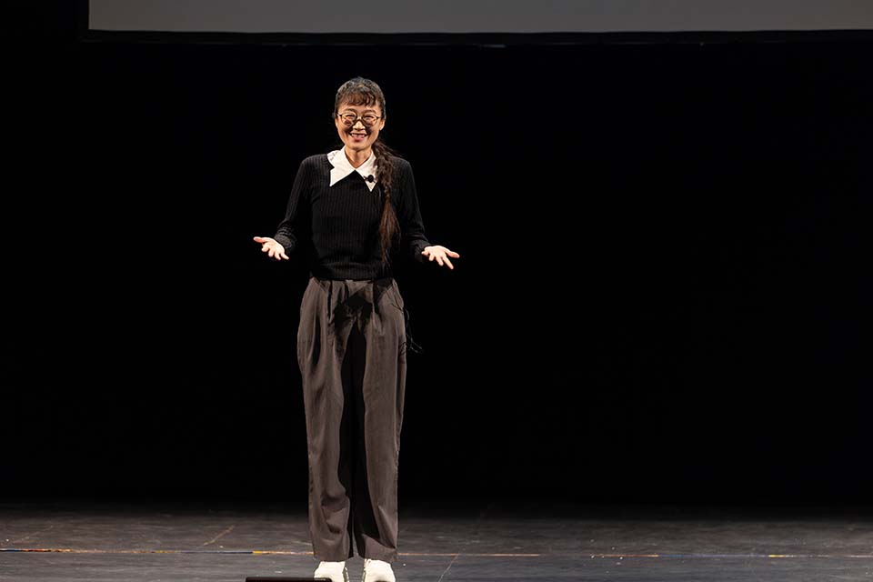 Jin Zhao stands onstage, facing the audience.