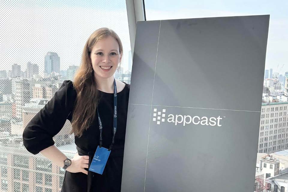Liz Mahon stands next to an Appcast sign in front of a window.