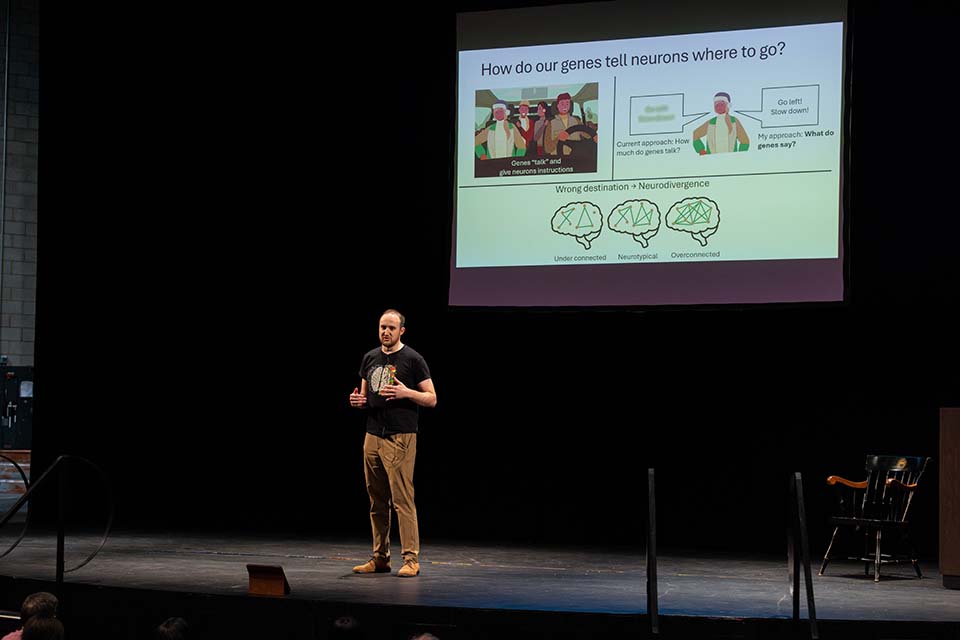 Ryan Gossart stands onstage presenting in front of a slide.