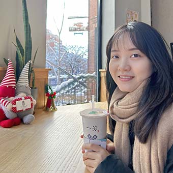 Shasha Yang sits at a table holding a beverage.