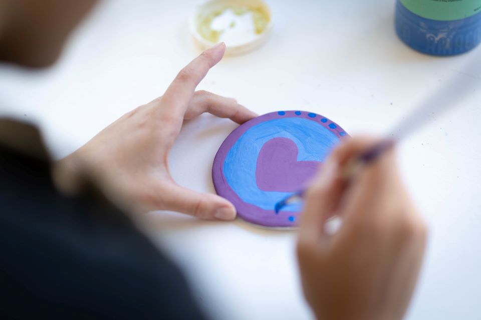 A student paints a heart on a coaster.