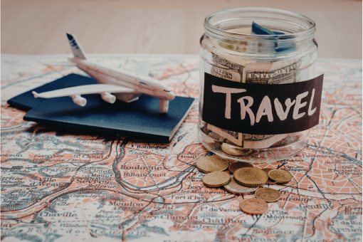 Jar of money labeled "travel" atop map and next to mini airplanes