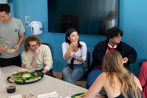 Students sit around a table eating lunch.