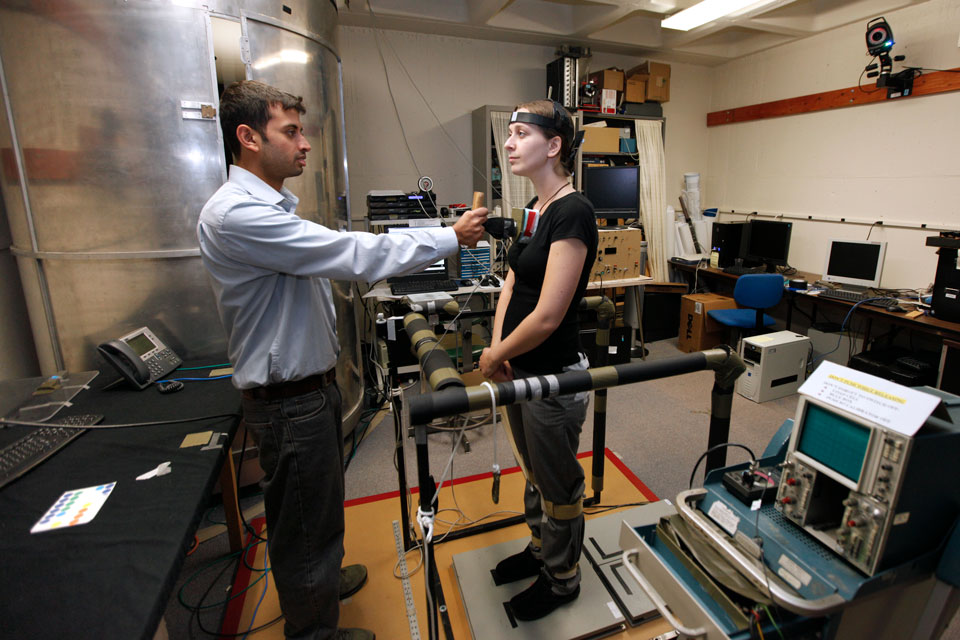 A research subject stands on the force platform while a researcher works on a computer.