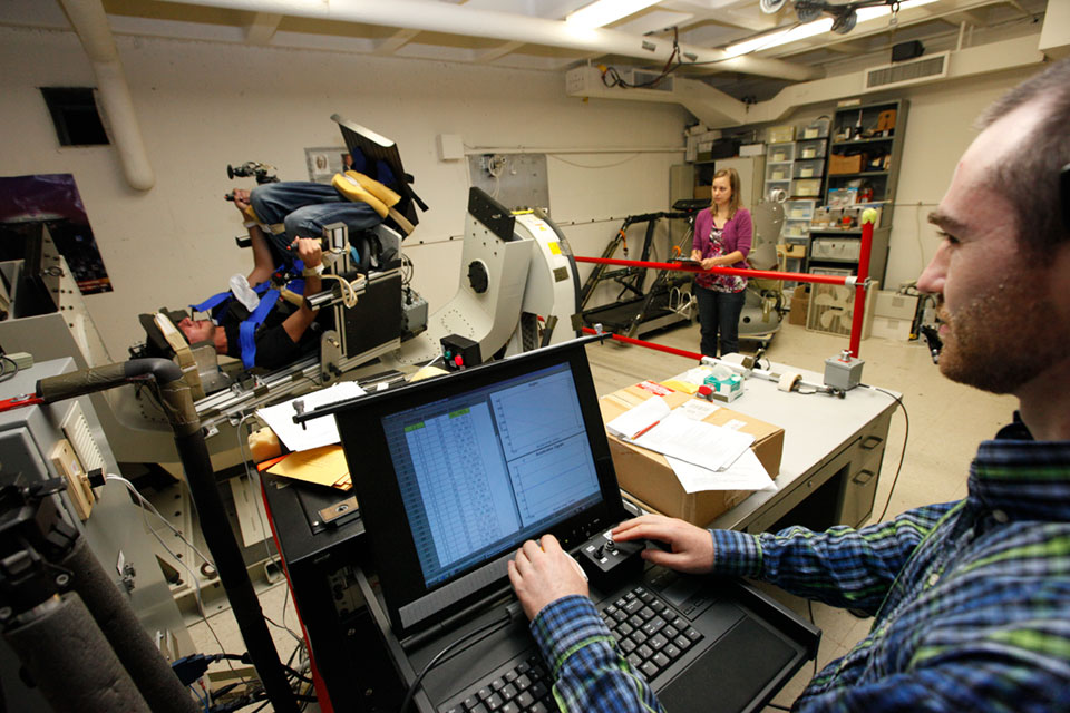 A research subject sits in a rotating chair  while two researchers look on.