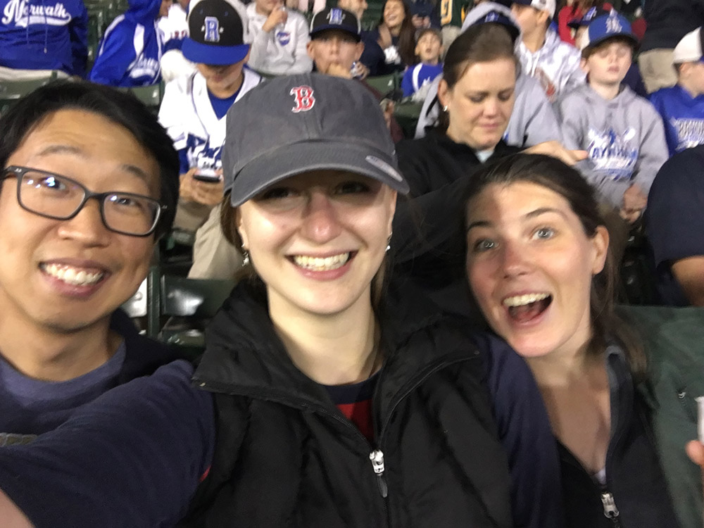 Janna Lowensohn and two colleagues smile in the stands at a baseball game.