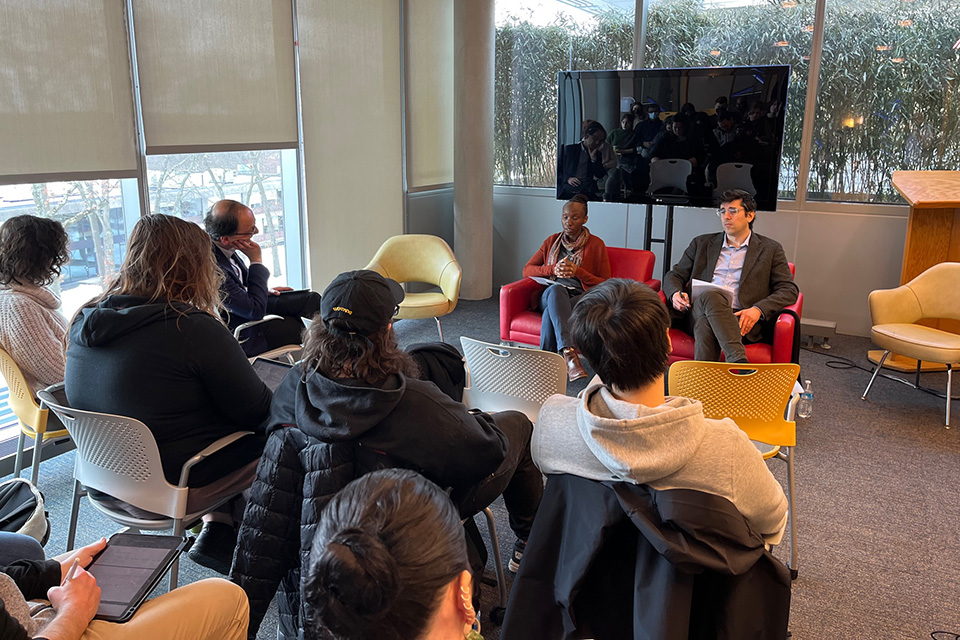 Wangui Muigai and Alex Kaye sit in chairs talking, facing a seated audience.