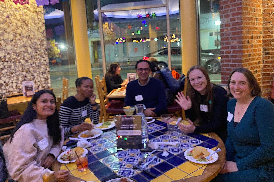 Students, alums, and staff sit together around a restaurant table.