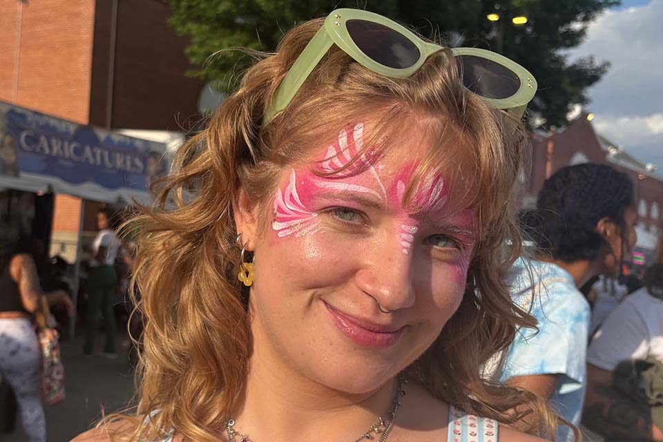 Photo of Cali McKenzie at a street fair, with pink butterfly face paint