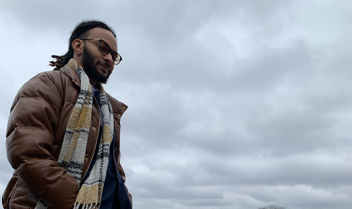 Image of Corey standing in front of dark clouds with a brown winter coat on.