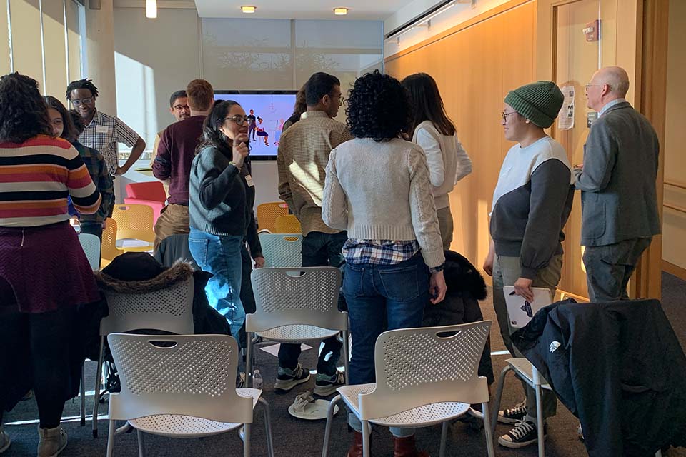 Thirteen people talk in small groups amongst rows of chairs.