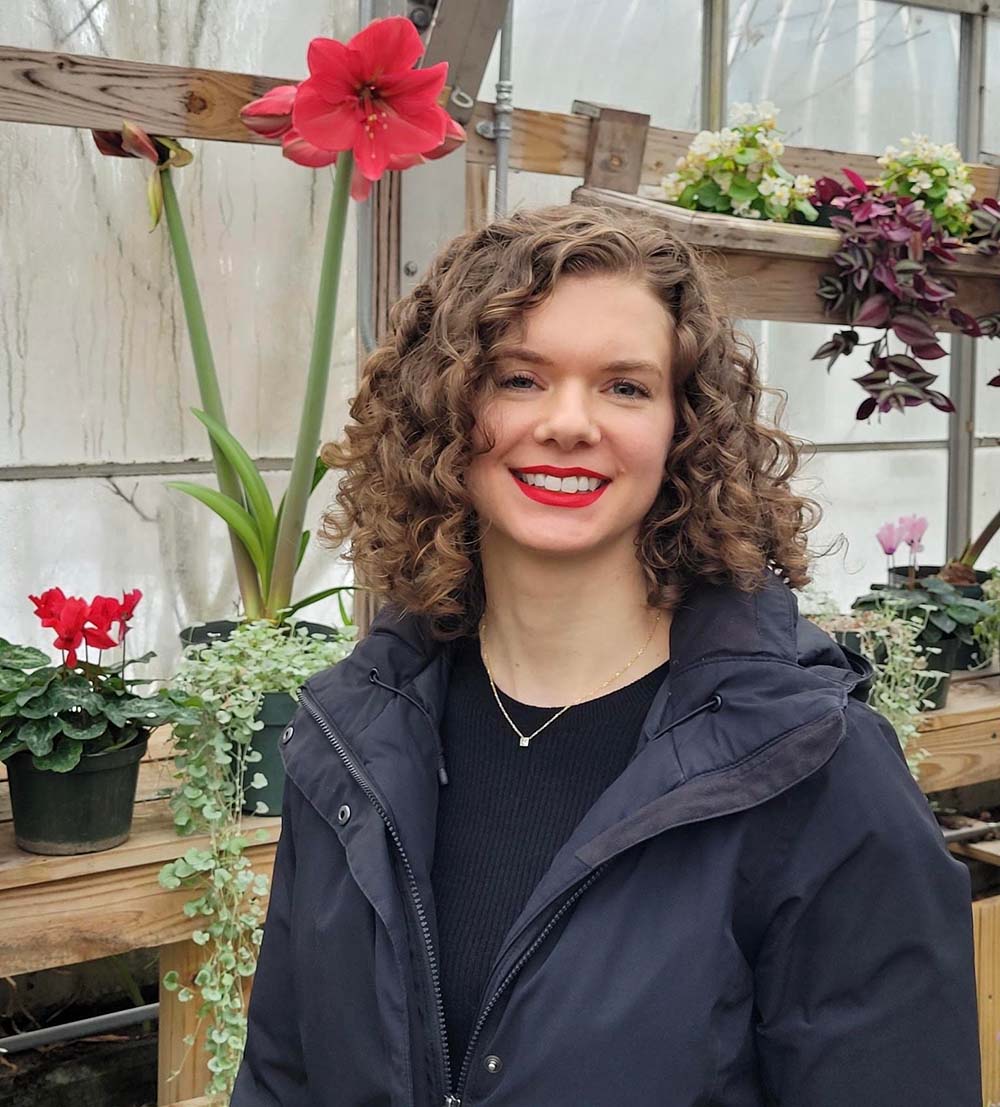 Claire Elling in front of colorful plants in a greenhouse.