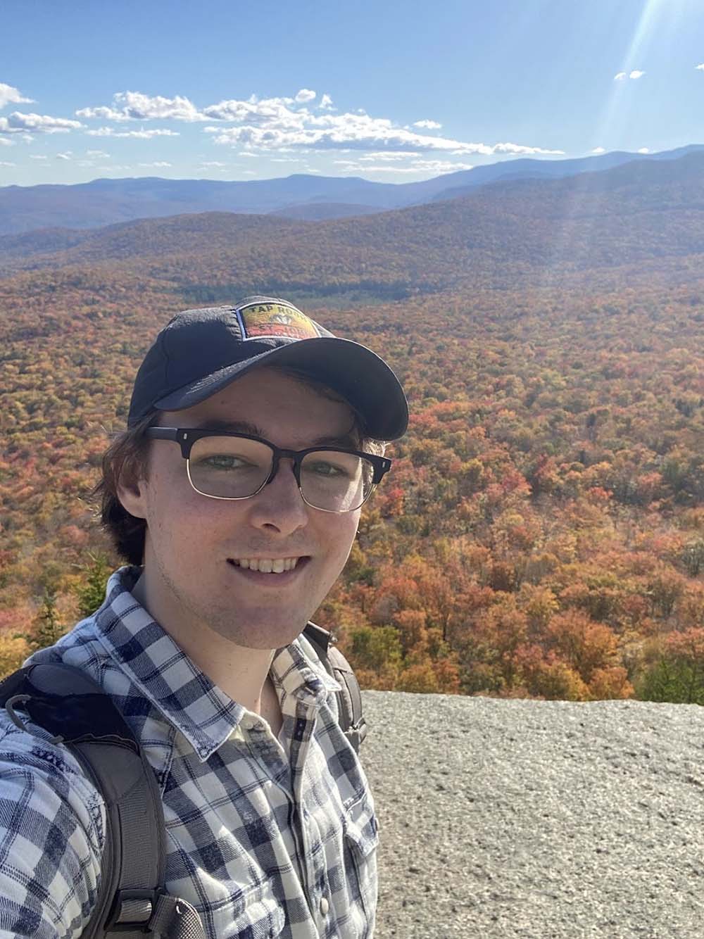 Hayden McCormick stands overlooking mountains and many autumn trees.