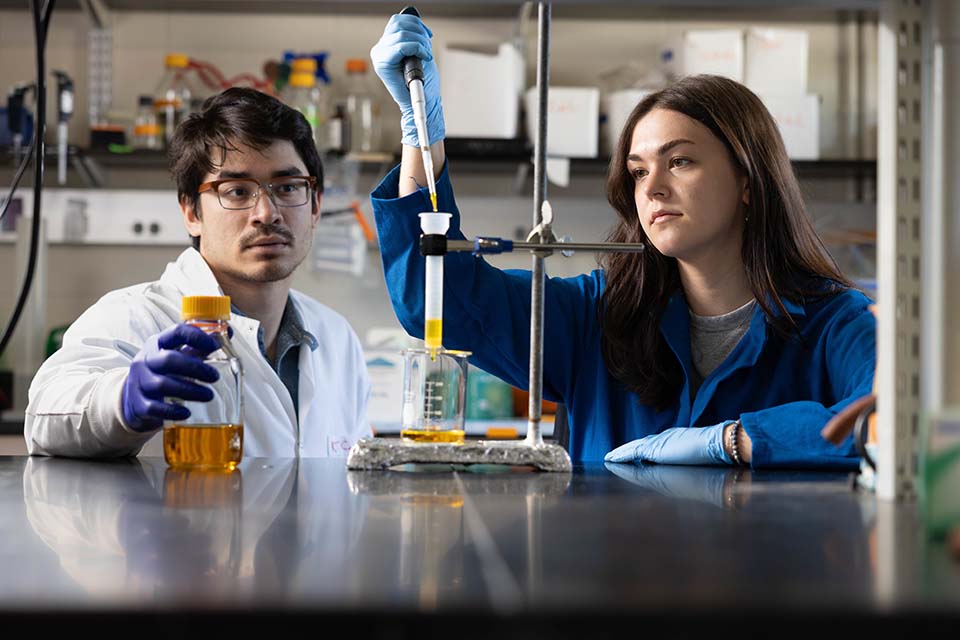 Two students work with pipettes in a lab.
