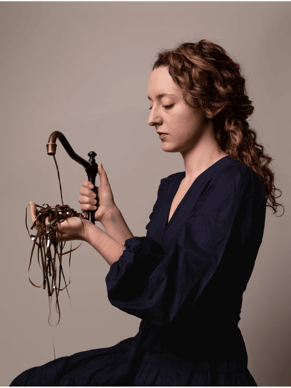  A young woman holds a metal faucet with analog magnetic tape overflowing into her hand.