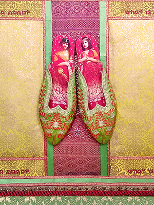 wall piece with patterned silk and slippers mounted in the middle. the outer most area is green silk with a floral pattern, then inside is a rose pink cord around it. the center background is a golden floral pattern, in the center behind the slipper is a vertical green and rose gold thick stripe pattern decoration. two photographic images young girls are cut in circular shape decorate each of the four corners of the golden floral background. the outside of the slipper has a green background with rose pink floral embroidery. inside of the slipper is rose pink background with two photographic image of two women in rose pink dresses.