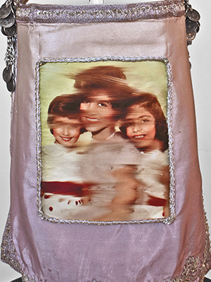 front view of a violet head piece sits on a pedestal. the head piece has two parts, they are attached on the side. the top part has emboridery decorated trhought out, silver decorations on the top, and photographic image of a gril superimposed on the top. the bottom part has silver deorations on the bottom and photographic image of a women and two children supermiposed in the middle