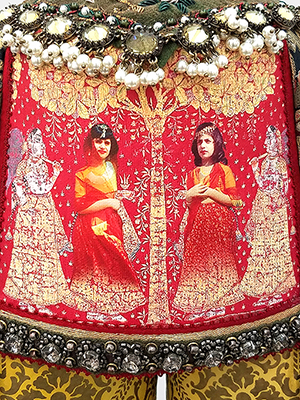 close up view of red fez cap in the sculpture shows two young girls in the center. the surface of the cap is covered with jewels