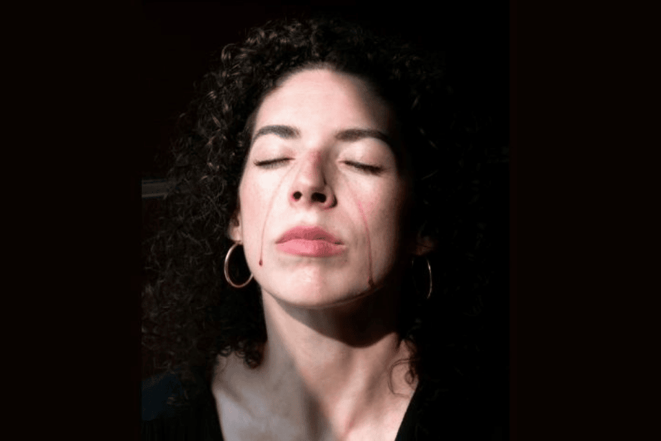 photograph of a woman's face with closed eyes and blood-red tears running down face. 