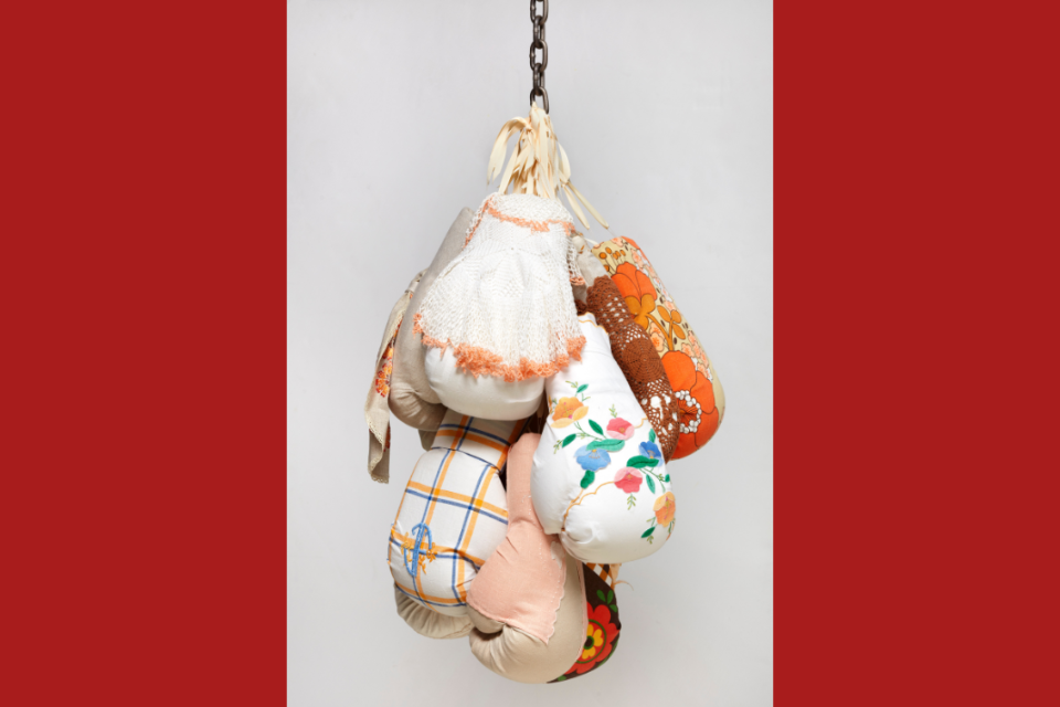 Stuffed oven mitts covered in decorative and lace linen made to look like boxing gloves, hanging from a chain to look like a punching bag