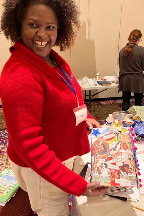 Shula Mola looking at the samples of art made by participants, boxes with cut out photos and images pasted inside and out.