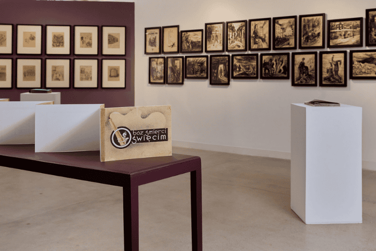 An art gallery with a handmade booklet in the foreground on a table and two collections of black and white drawings on the wall behind