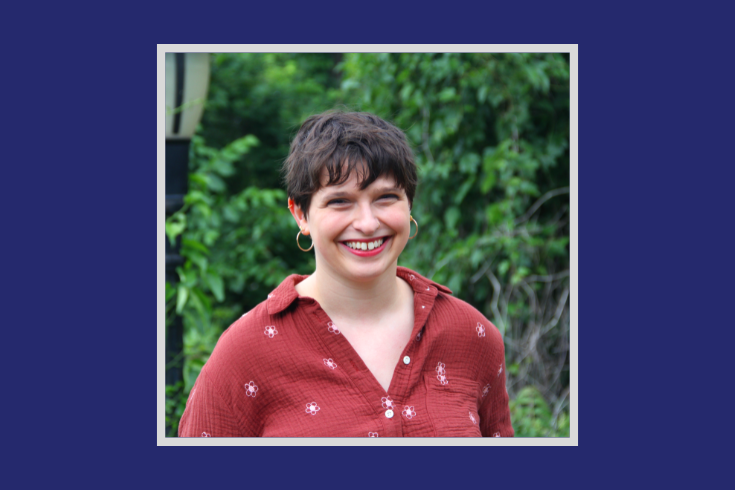 Avigayil Halpern - a White woman with short brown hair wearing a red blouse standing in front of a tree with green leaves.