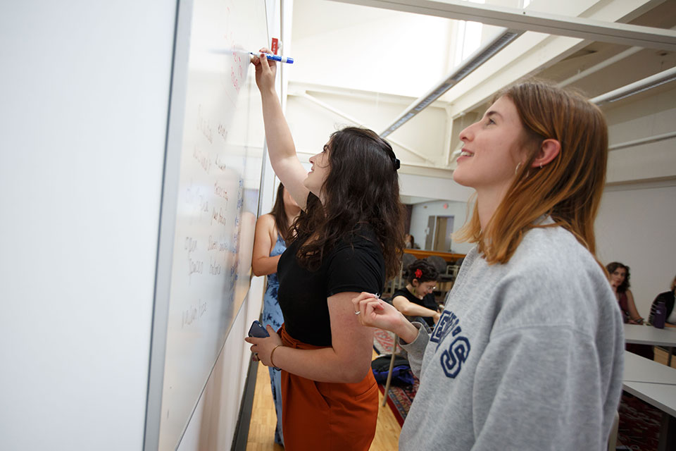 Students stand and write on a whiteboard