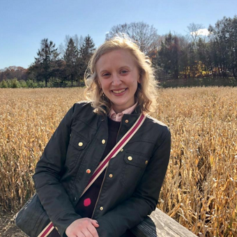 Samantha Pickette is a White woman wearing a black jacket, standing in front of a corn field