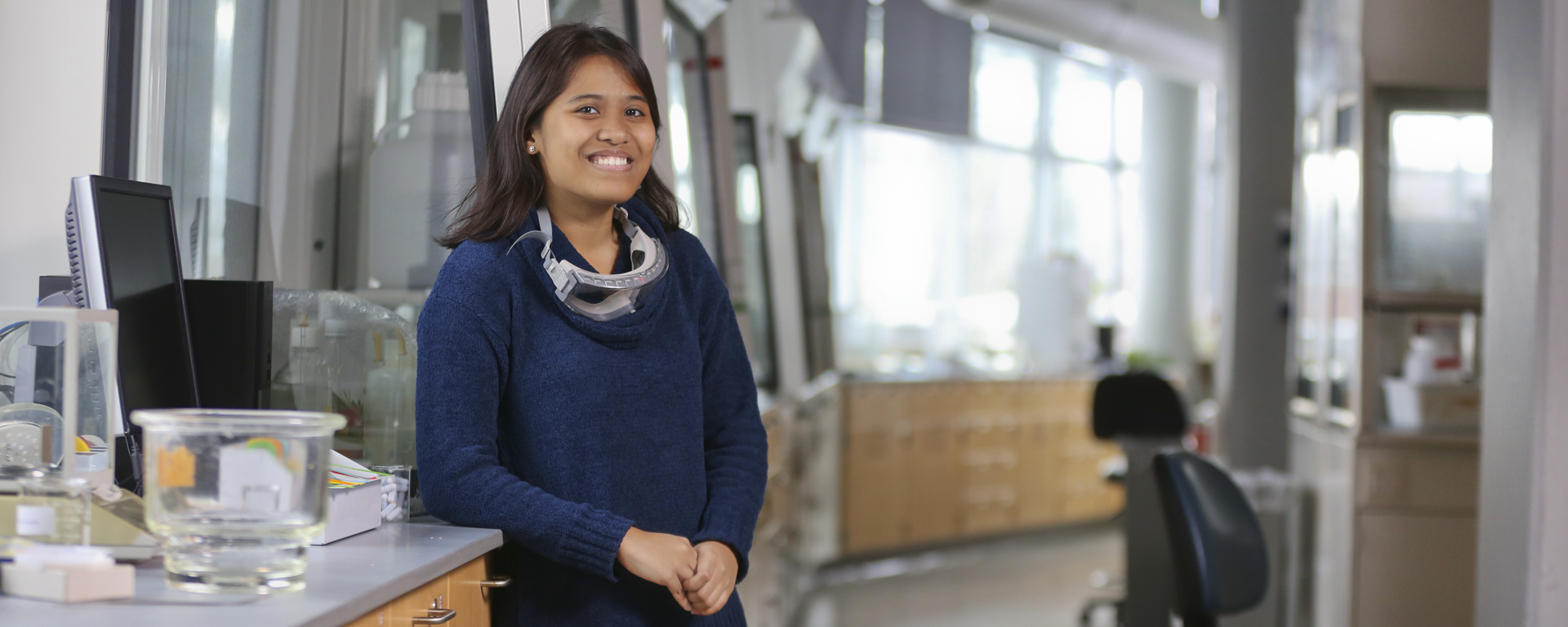 Mariel Guzman standing in a science lab with goggles draped around her neck
