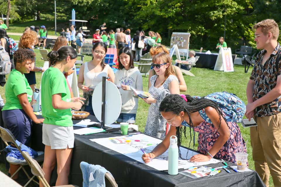 Students gather at the 9 Out of 10 booth and one signs the pledge banner