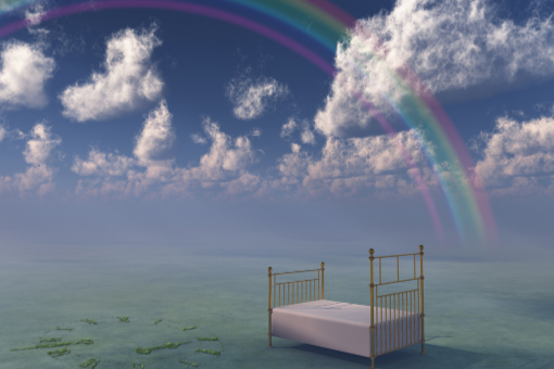 A bed sits in the ocean under a rainbow