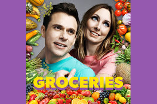 A man and woman smiling are surrounded by fruits and veggies