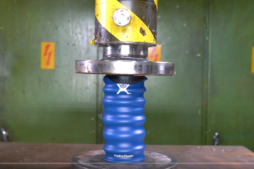 A Hydroflask bottle being crushed in a hydraulic press