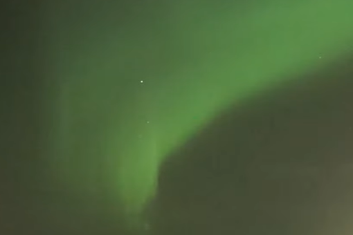 Screenshot from a live stream of the Northern Lights with the image showing a green streak through the night sky