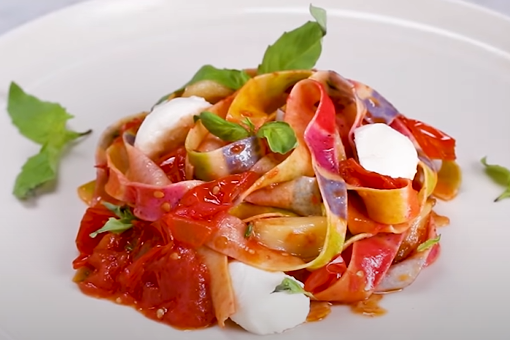 Screenshot from video with image of pasta with yellow, purple, and red and noodles, tomato sauce, ricotta cheese, and basil