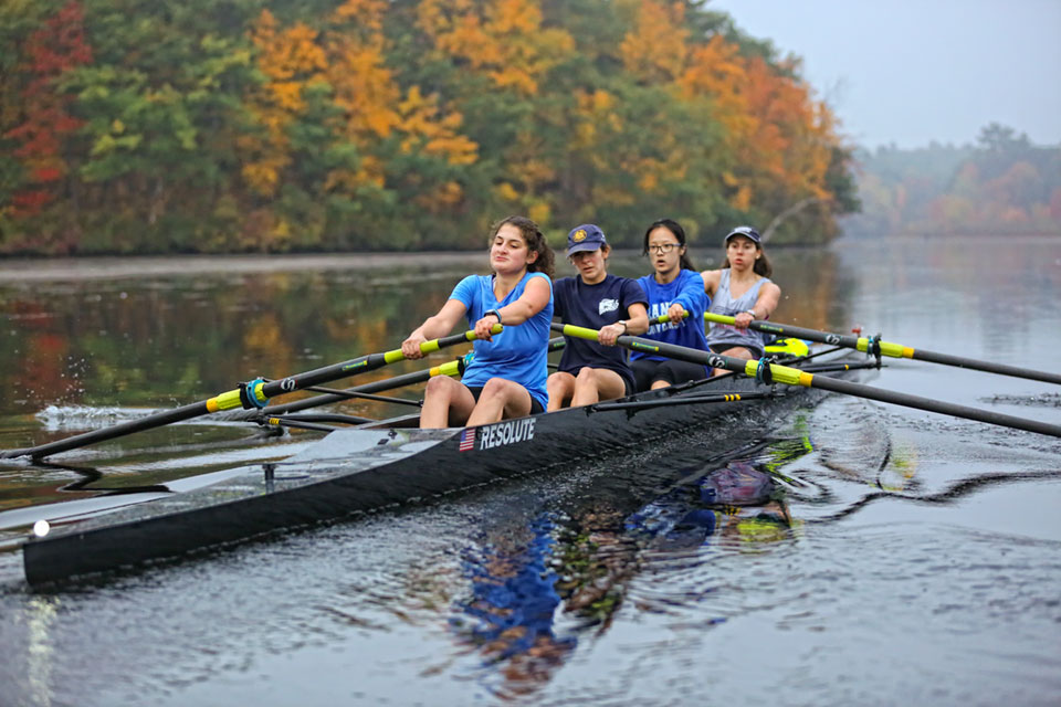 Four students row down the river in a shell