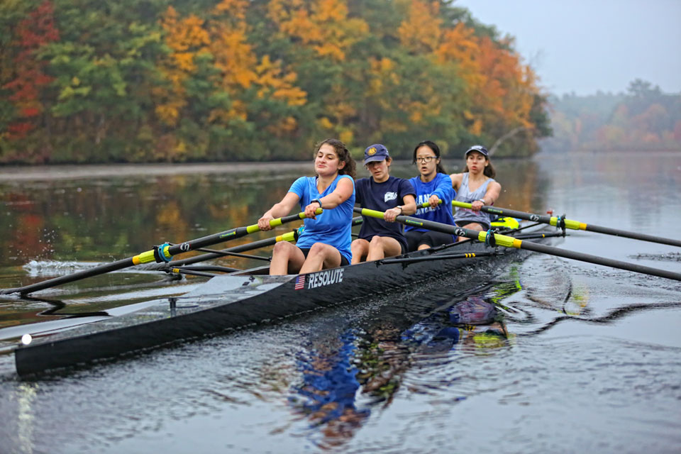 Four students row down the river in a shell