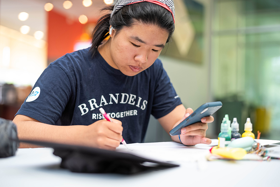 Emily Su ’23, sketches out a design she will use to adorn her mortarboard for her upcoming commencement ceremony during a graduation cap decoration event at the Shapiro Campus Center on May 16, 2023. Photo/Gaelen Morse