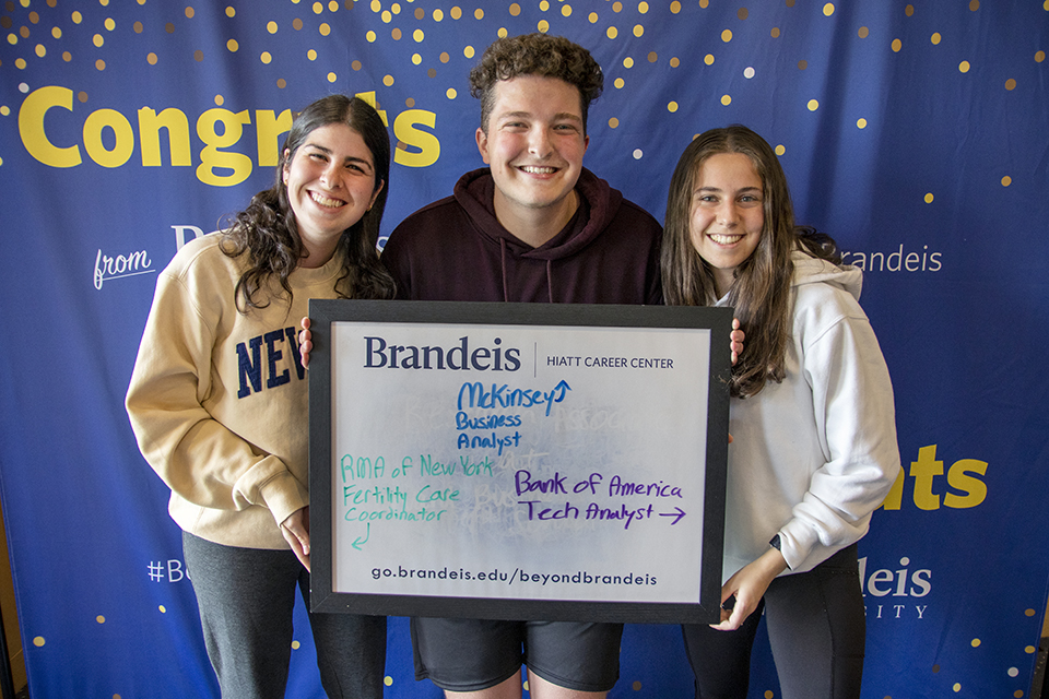 Students post with a whiteboard that reads, "McKinsey Business Analyst, RMA of NY Fertility Care Coordinator, and Bank of America Tech Analyst"