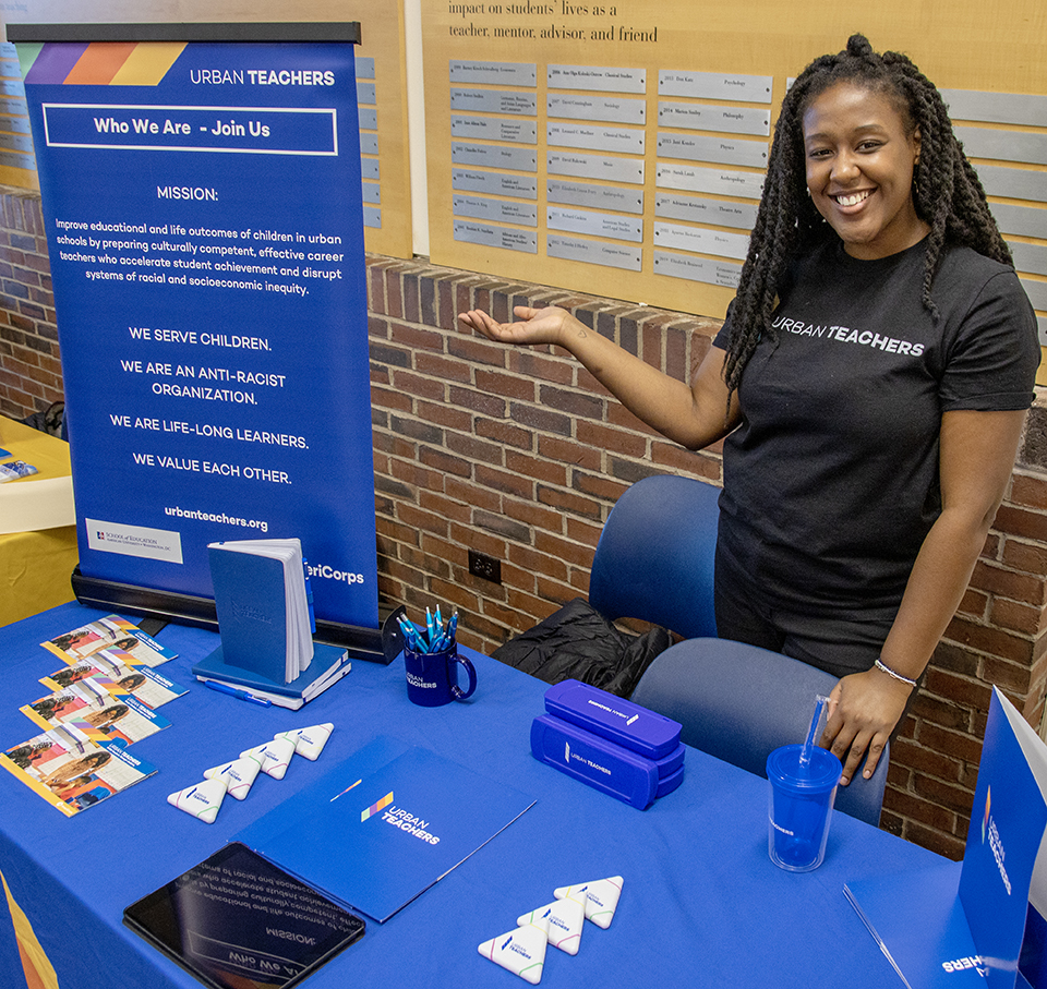 A recruiter poses with their table at a career fair.