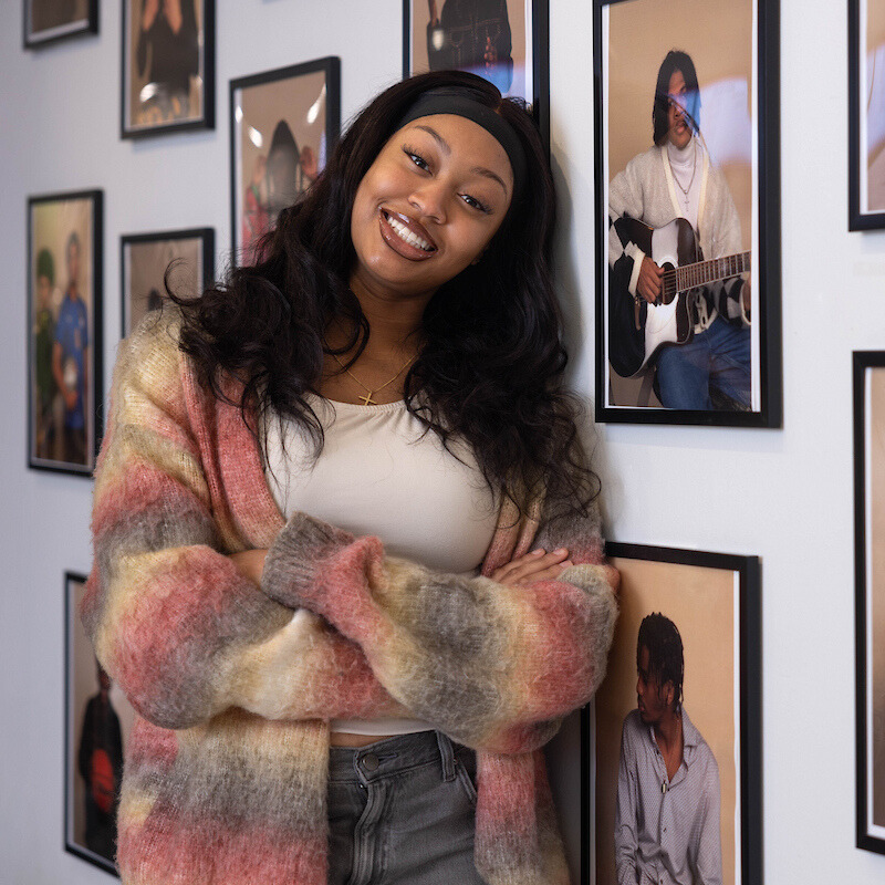 Efosa Ologbosere ‘27 poses for a photo next to her photography exhibit titled “Love, Black Men” in Usdan Student Center at Brandeis University.