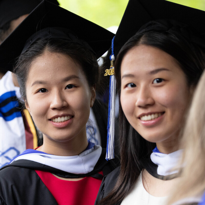 Two students in graduation caps and gowns smile at camera.