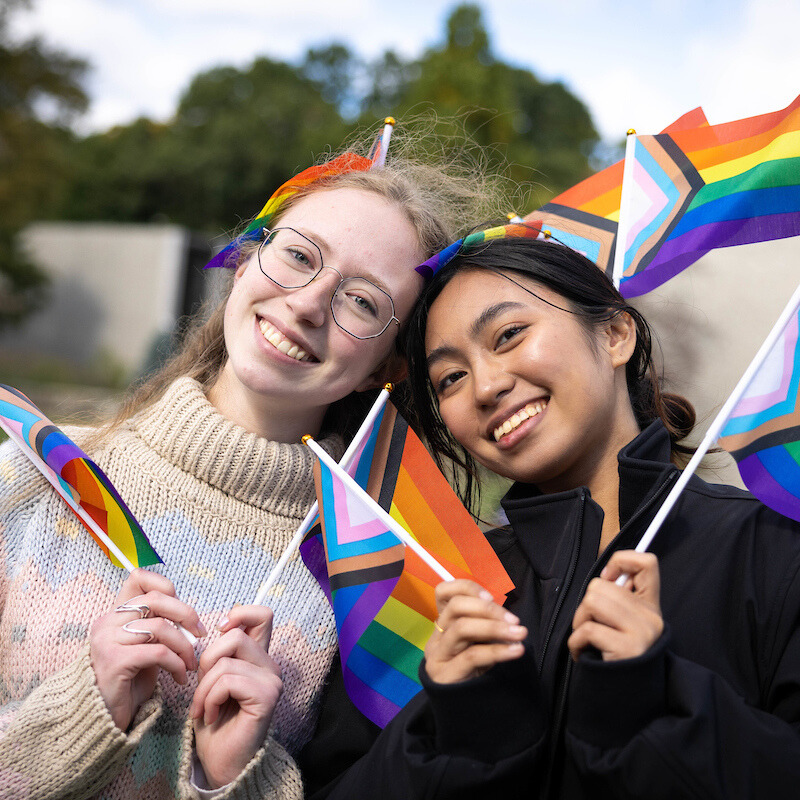 Two Brandeis students at 2024 pride celebration, holding rainbow flags.