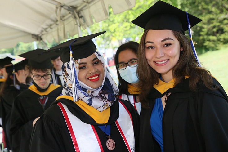 Two Class of 2022 students in graduation regalia pose for a photo before entering the commencement ceremony.