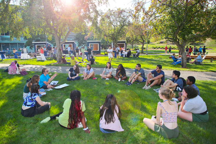 Students sits in a circle with their orientation leader outside the Shapiro Campus Center.