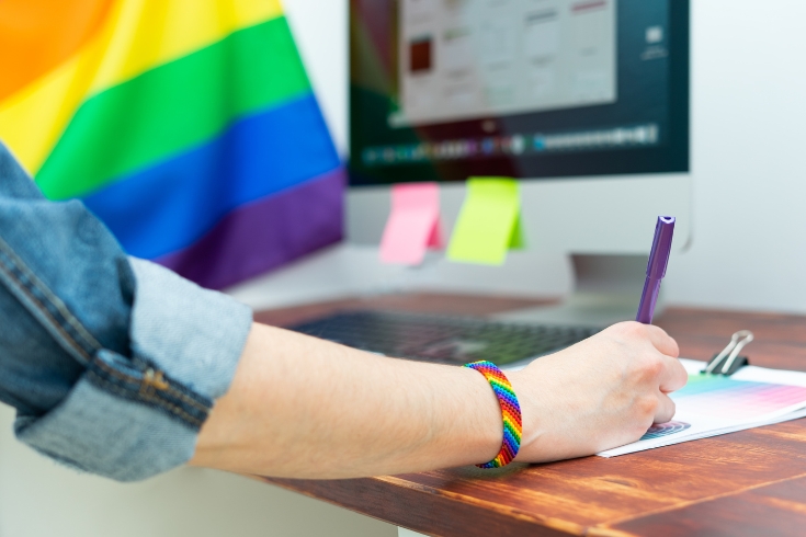 A person works at their office desk alongside LGBTQI+ pride colors.