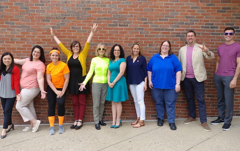Group of adults in colorful clothing stand and cheer.